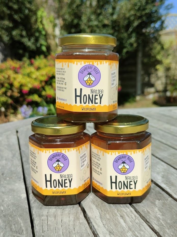 Three jars of Dewberry Bees honey stacked on a garden table